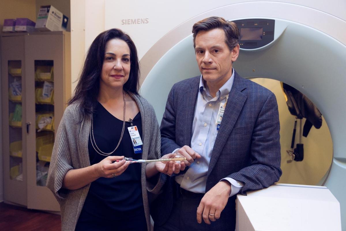 Dr. Shayna and Tim Showalter are shown standing in front of a radiation machine.